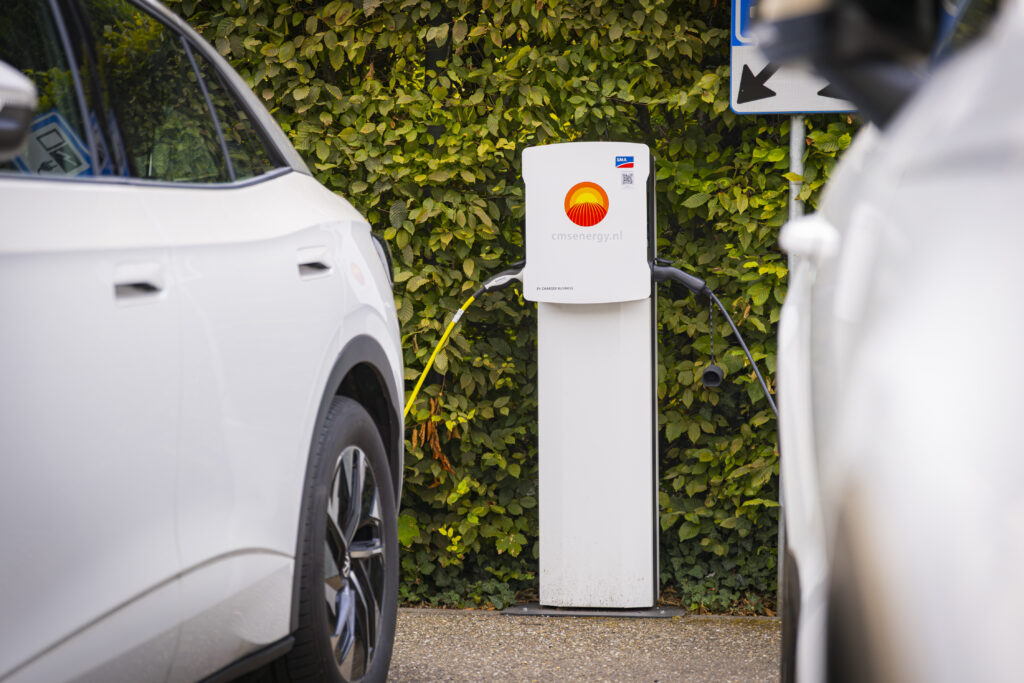 Witte elektrische auto aangesloten op een laadpaal van cmsenergy.nl bij hotel Vaeshartelt met groene haag op de achtergrond